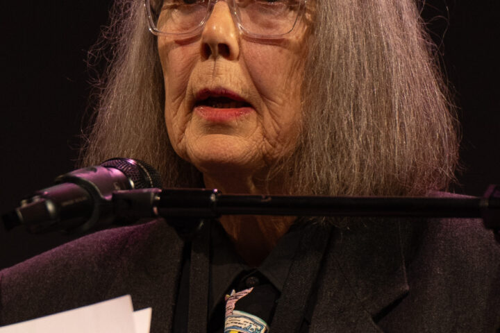 Anne Carson spricht an einem Mikrofon auf einer Bühne.