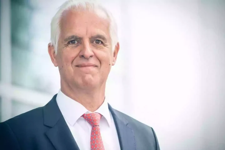 Porträt eines älteren Mannes im Anzug mit roter Krawatte vor hellem Hintergrund.