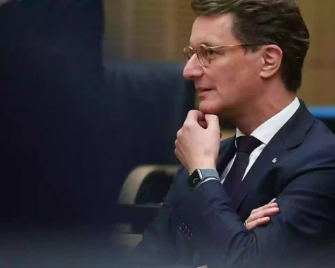 Hendrik Wüst sitzt in einem Sitzungssaal und blickt nach vorn, die Hand am Kinn.