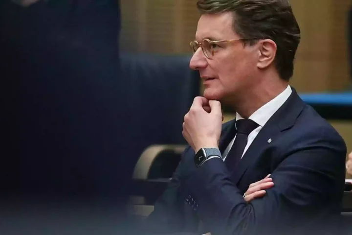 Hendrik Wüst sitzt in einem Sitzungssaal und blickt nach vorn, die Hand am Kinn.