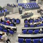 Blick in den Plenarsaal des Deutschen Bundestags mit Abgeordneten an den Plätzen und einer Person am Rednerpult.