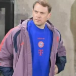 Ein Mann im FC-Bayern-Outfit steht vor einem Gebäude und blickt zur Seite.