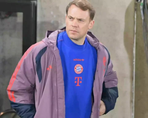 Ein Mann im FC-Bayern-Outfit steht vor einem Gebäude und blickt zur Seite.