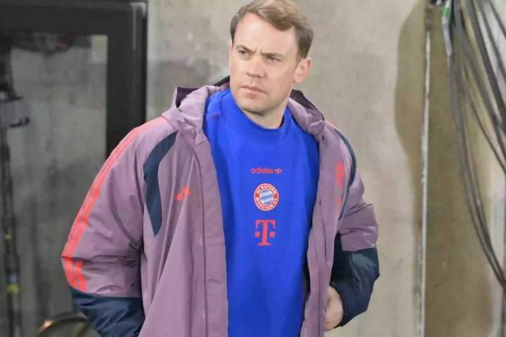 Ein Mann im FC-Bayern-Outfit steht vor einem Gebäude und blickt zur Seite.