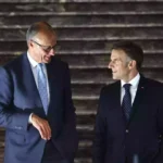 Zwei Politiker in dunklen Anzügen stehen nebeneinander und sprechen miteinander.