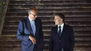 Zwei Politiker in dunklen Anzügen stehen nebeneinander und sprechen miteinander.