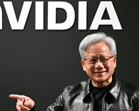 Ein Mann steht vor einem großen Nvidia-Logo und zeigt mit der Hand zur Seite.