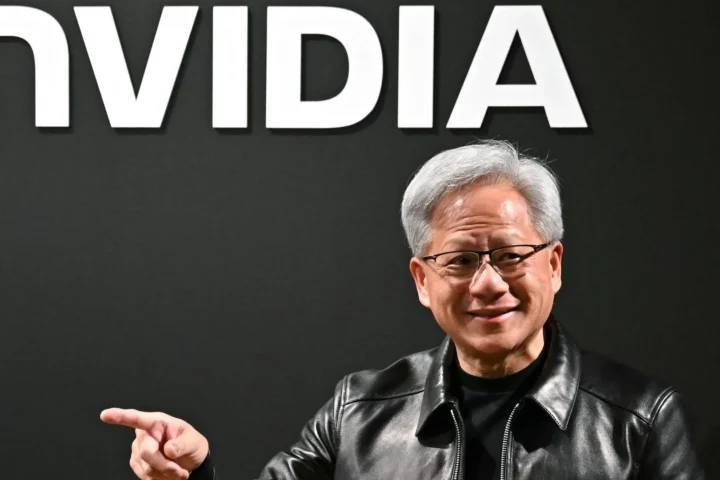 Ein Mann steht vor einem großen Nvidia-Logo und zeigt mit der Hand zur Seite.