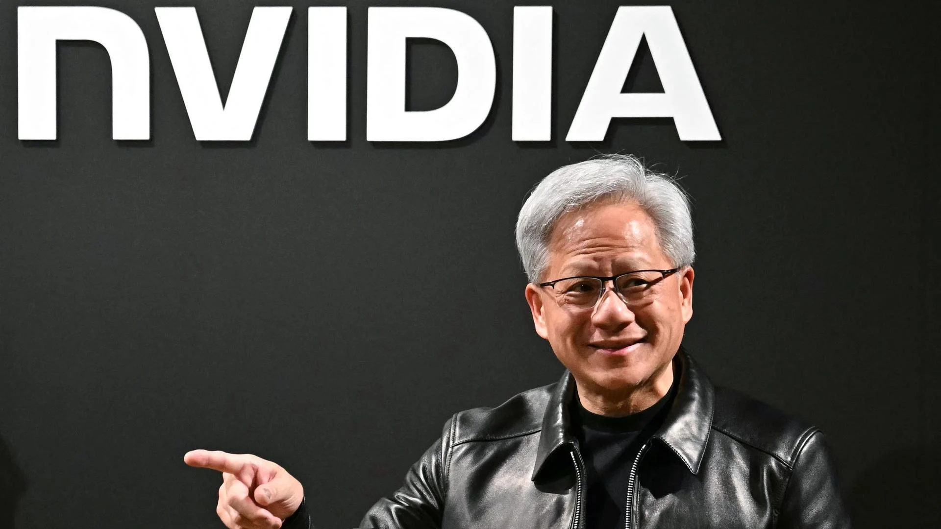 Bundesregierung plant Partnerschaft mit Nvidia für KI in der Industrie 1 Ein Mann steht vor einem großen Nvidia-Logo und zeigt mit der Hand zur Seite.