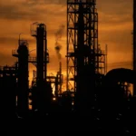 Silhouette einer Raffinerie bei Sonnenuntergang mit Schloten und Industrieanlagen.