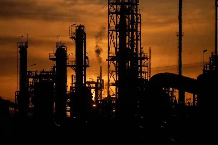 Silhouette einer Raffinerie bei Sonnenuntergang mit Schloten und Industrieanlagen.