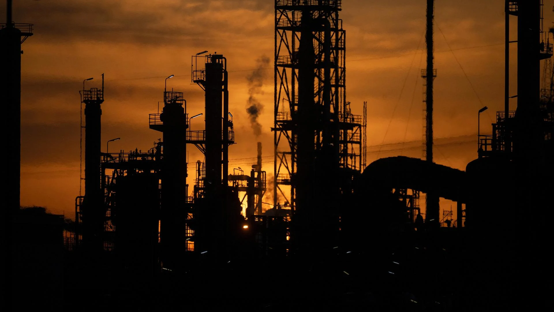 Silhouette einer Raffinerie bei Sonnenuntergang mit Schloten und Industrieanlagen.