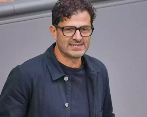 Ein Mann mit Brille und dunkler Jacke vor grauem Hintergrund.