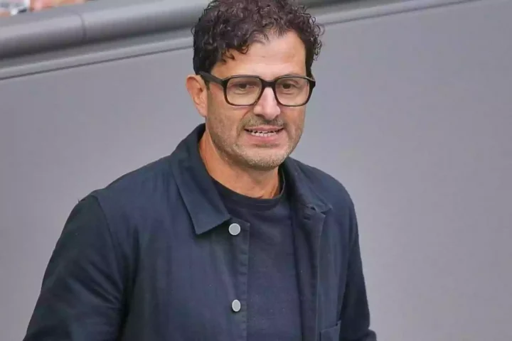 Ein Mann mit Brille und dunkler Jacke vor grauem Hintergrund.
