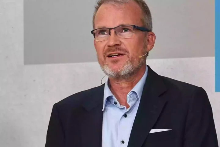 Jens Baas spricht bei einem Auftritt mit Mikrofon-Headset und dunklem Sakko.