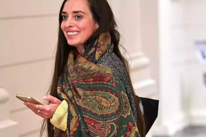 Vanessa Emde lächelt in einem Innenraum und hält ein Smartphone in der Hand.