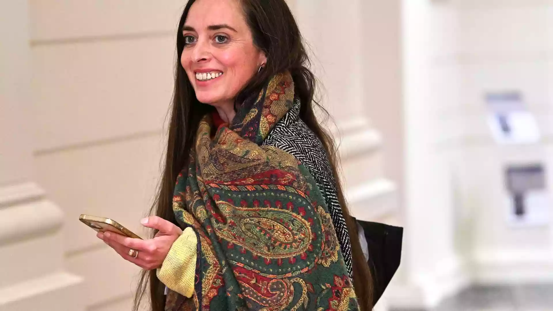 Vanessa Emde lächelt in einem Innenraum und hält ein Smartphone in der Hand.