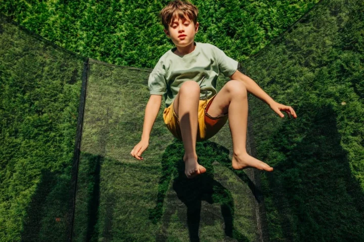 Ein Junge springt auf einem Trampolin im Garten.