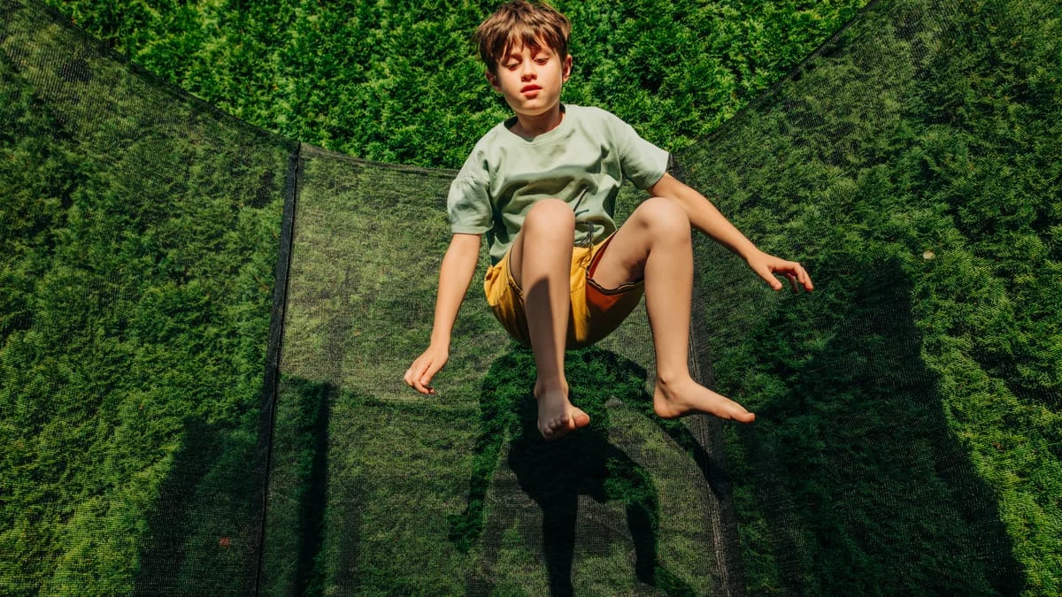 Ein Junge springt auf einem Trampolin im Garten.